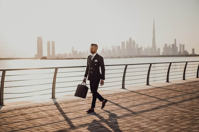 A manager in the Middle East walking on a coatline, opposite skyscrapers and the coast