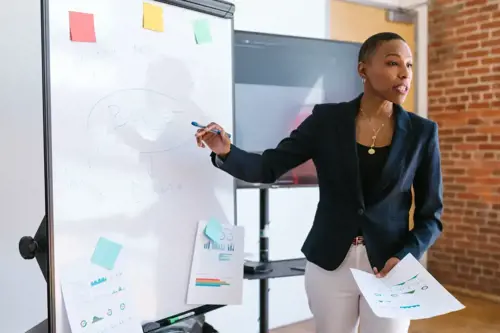 A woman of colour pointing at a whiteboard
